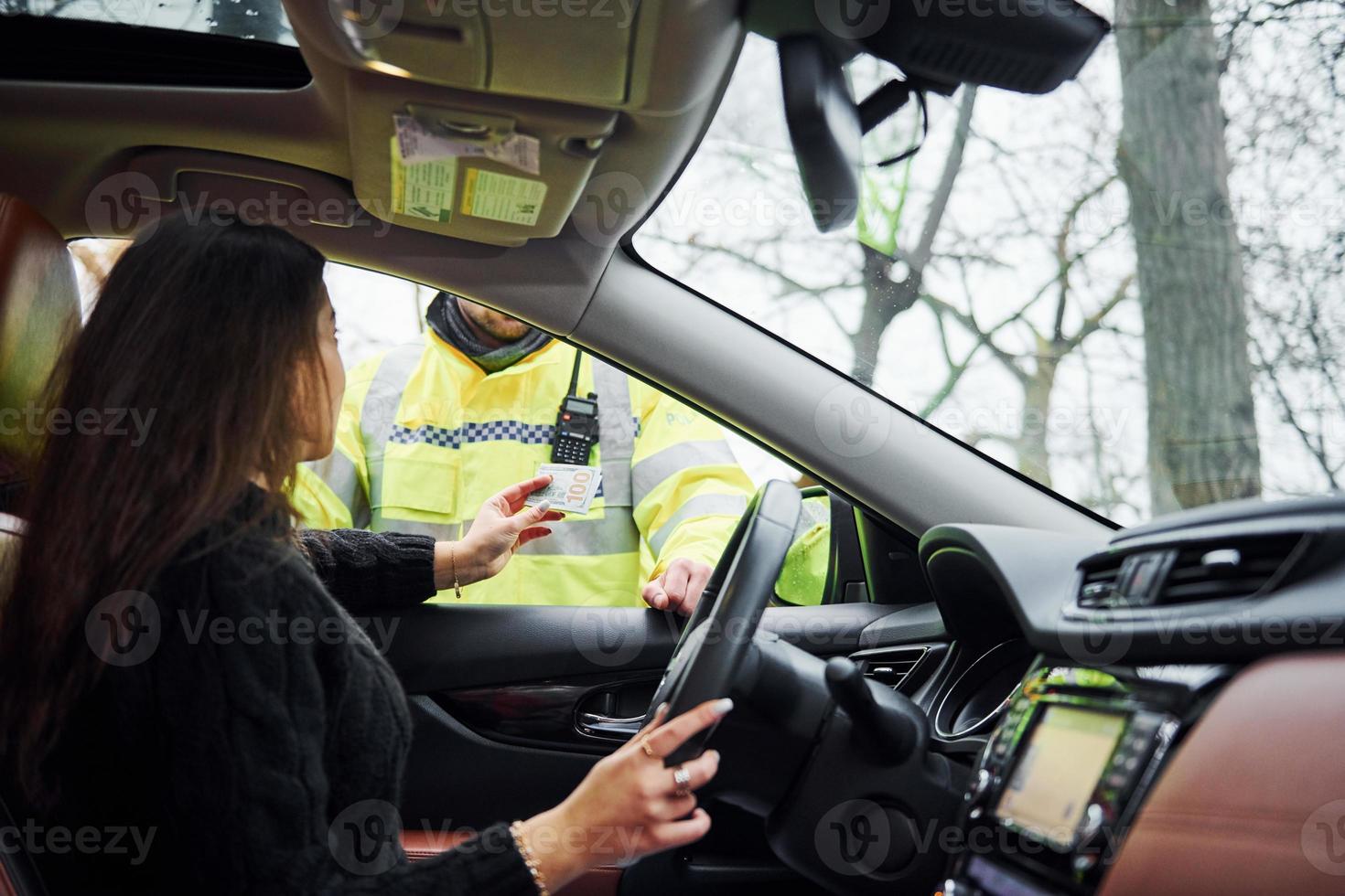 manlig polis officer i grön enhetlig kontroll fordon på de väg. kvinna påfrestande till ge muta foto