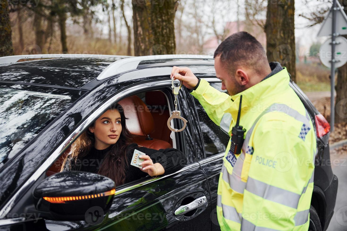 manlig polis officer i grön enhetlig och med handklovar vägra till ta muta från kvinna i fordon foto