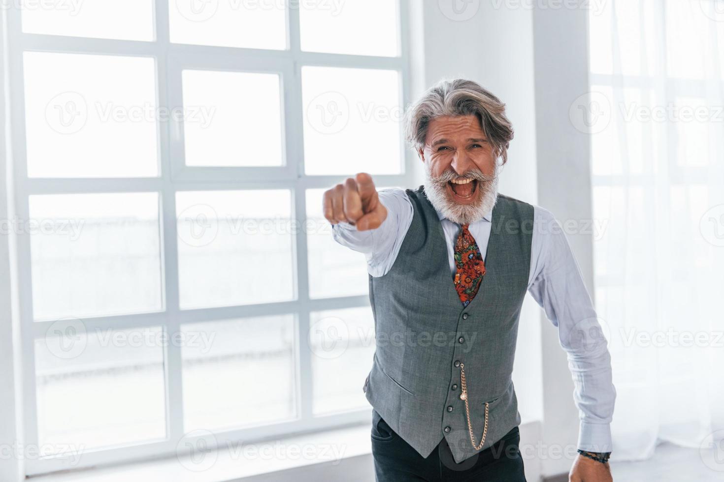 skrikande senior man i jacka och slips inomhus i rum mot fönster foto