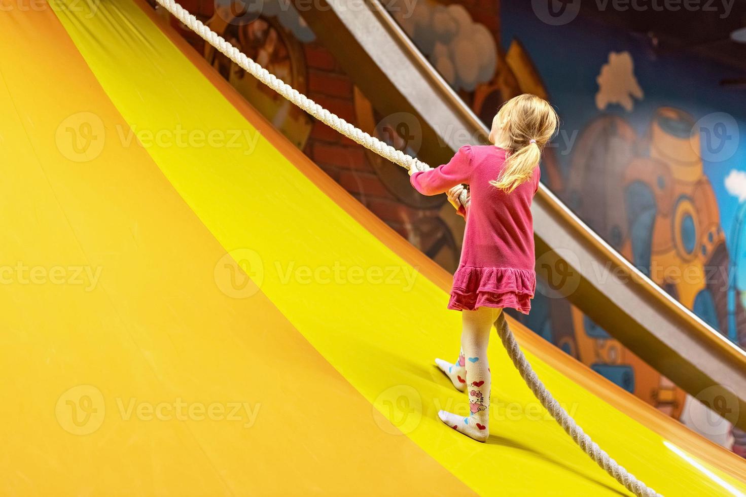 de litet barn flicka klättrar de rep på de glida. lekplats, Lycklig barndom foto