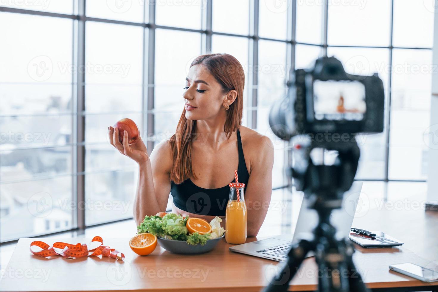 kvinna vlogger med sportigt kropp stående inomhus nära tabell med friska mat foto