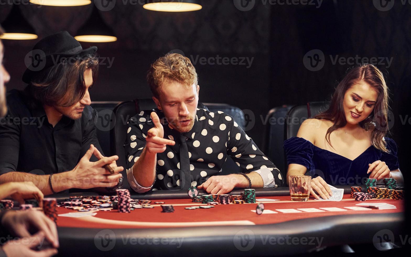 med glasögon av dryck. grupp av elegant ung människor den där spelar poker i kasino tillsammans foto