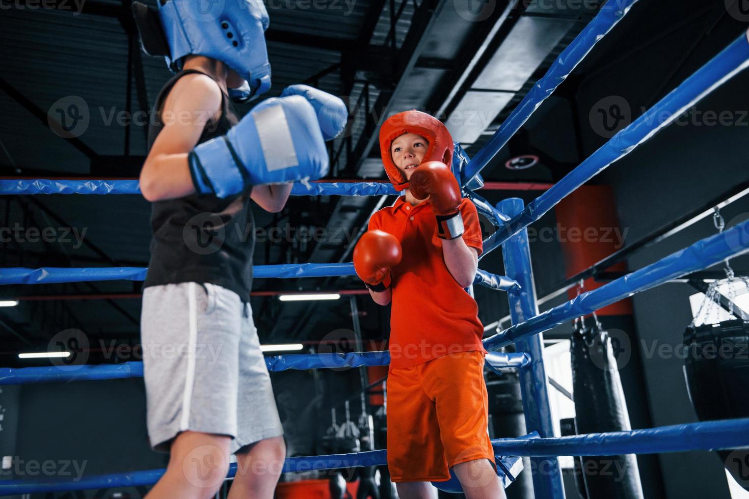 två Pojkar i skyddande Utrustning ha sparring och stridande på de boxning ringa foto