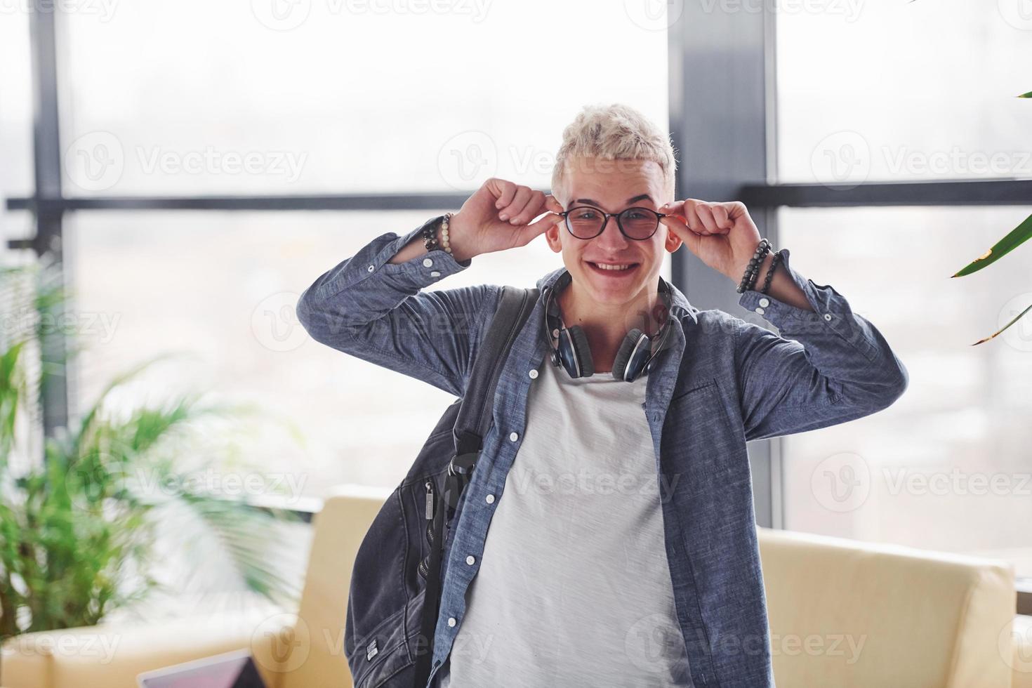 leende hipster kille i glasögon och med ryggsäck står inomhus foto