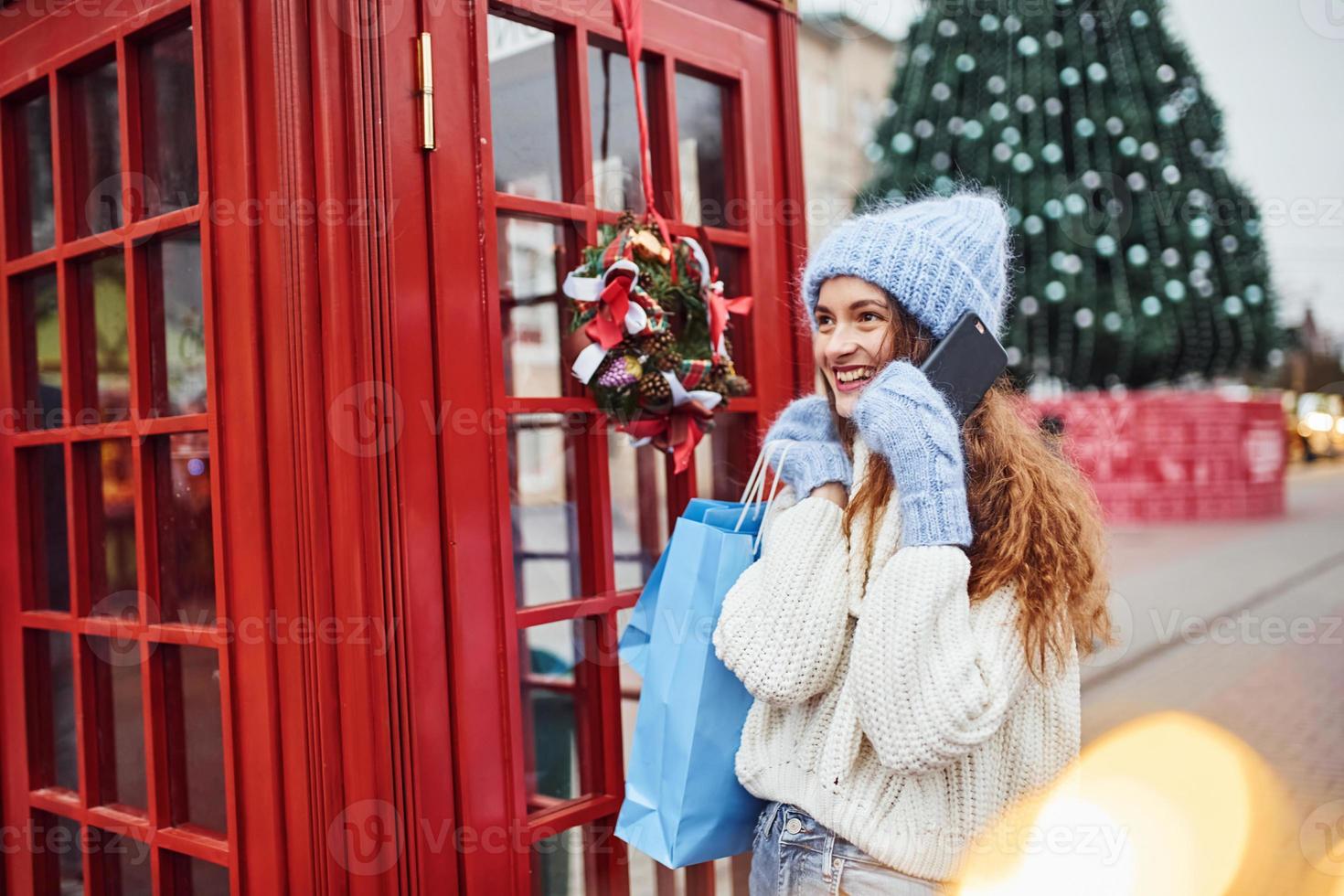 ung flicka i värma kläder ha en promenad utomhus i de stad nära röd telefon station foto
