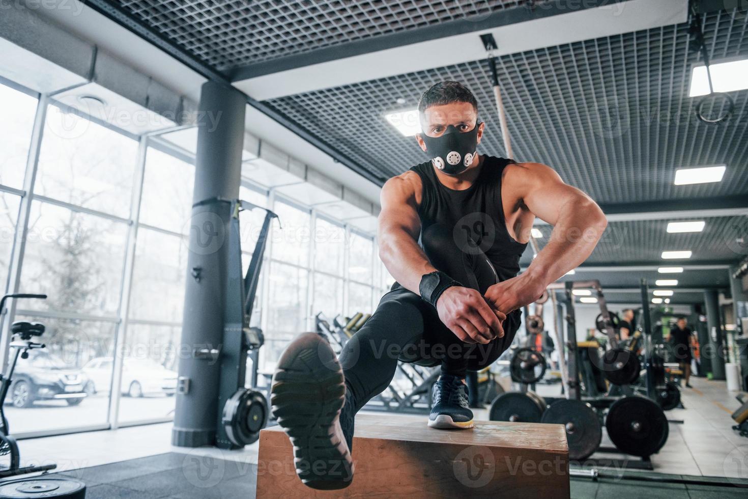 stark ung man i sportigt kläder och skrämmande mask håller på med skjuta på Posten på ett ben i Gym foto