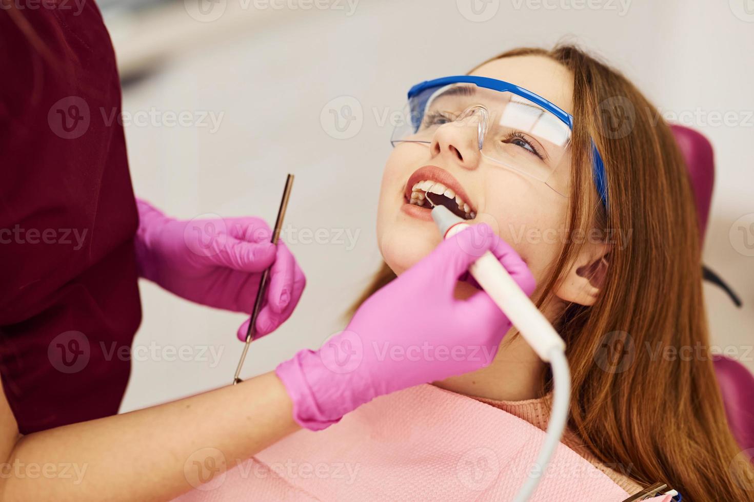 liten flicka i skyddande glasögon besöker tandläkare i klinik. uppfattning av stomatologi foto