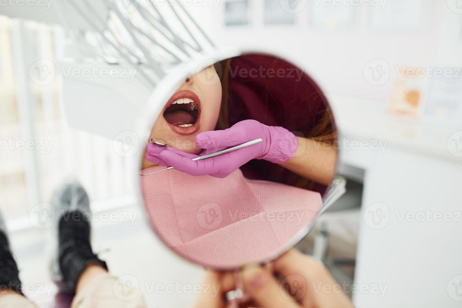 utseende på spegel. liten flicka besöker tandläkare i klinik. uppfattning av stomatologi foto