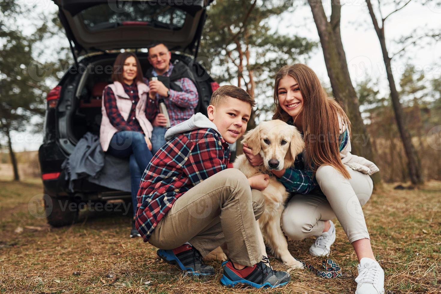 Lycklig familj Sammanträde och har roligt med deras hund nära modern bil utomhus i skog foto