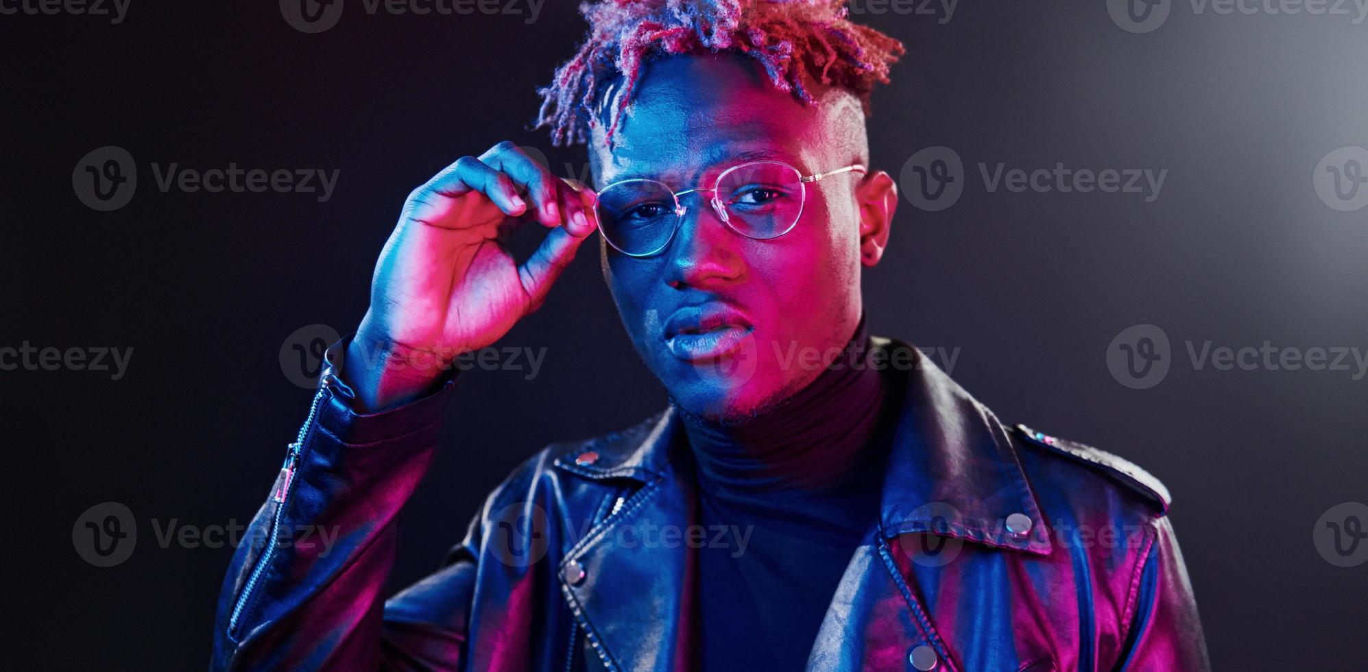 trogen neon belysning. ung afrikansk amerikan man i glasögon stående i studio foto