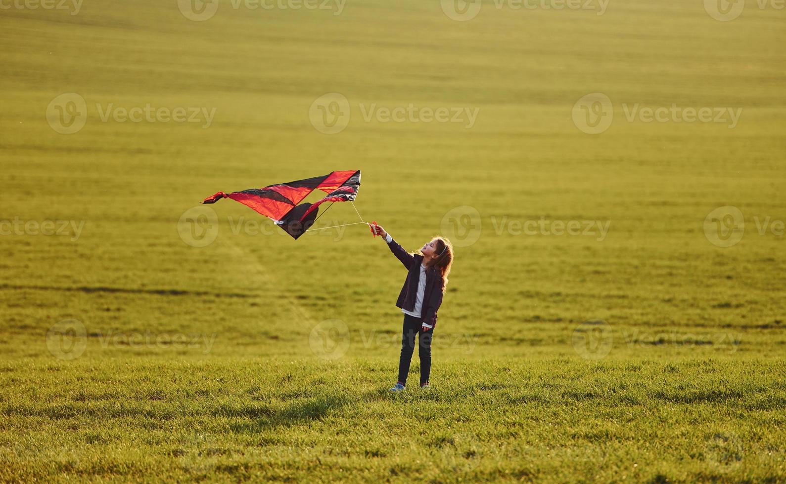 Lycklig liten flicka löpning med drake i händer på de skön fält foto