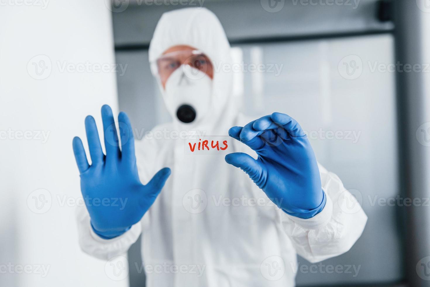 manlig läkare forskare i labb täcka, defensiv glasögon och mask innehar glas med virus ord på den foto