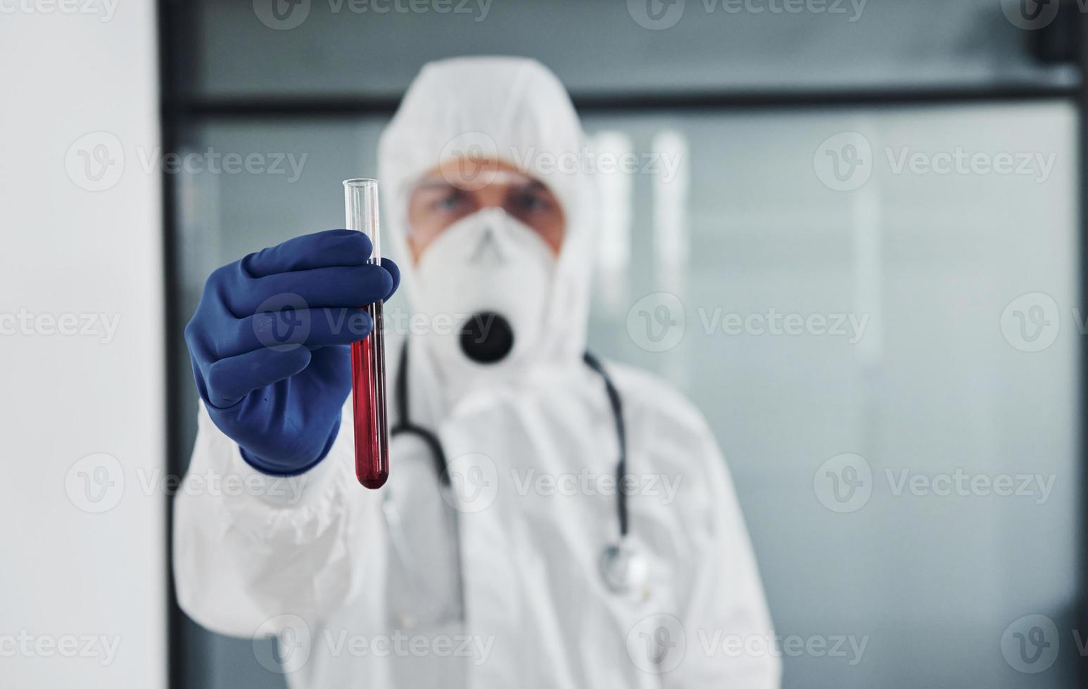 manlig läkare forskare i labb täcka, defensiv glasögon och mask innehar testa rör med blod foto
