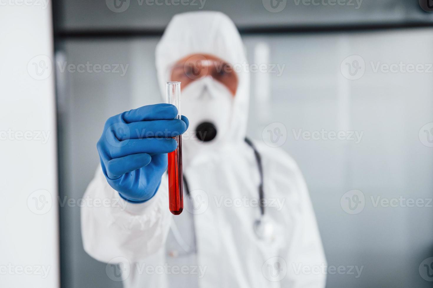 manlig läkare forskare i labb täcka, defensiv glasögon och mask innehar testa rör med blod foto