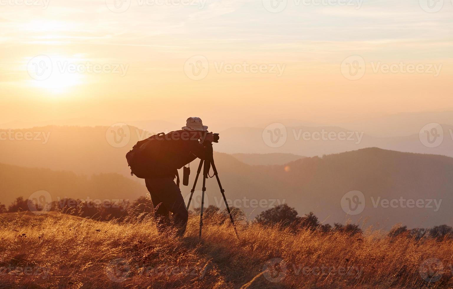 manlig fotograf stående och arbetssätt på majestätisk landskap av höst träd och bergen förbi de horisont foto