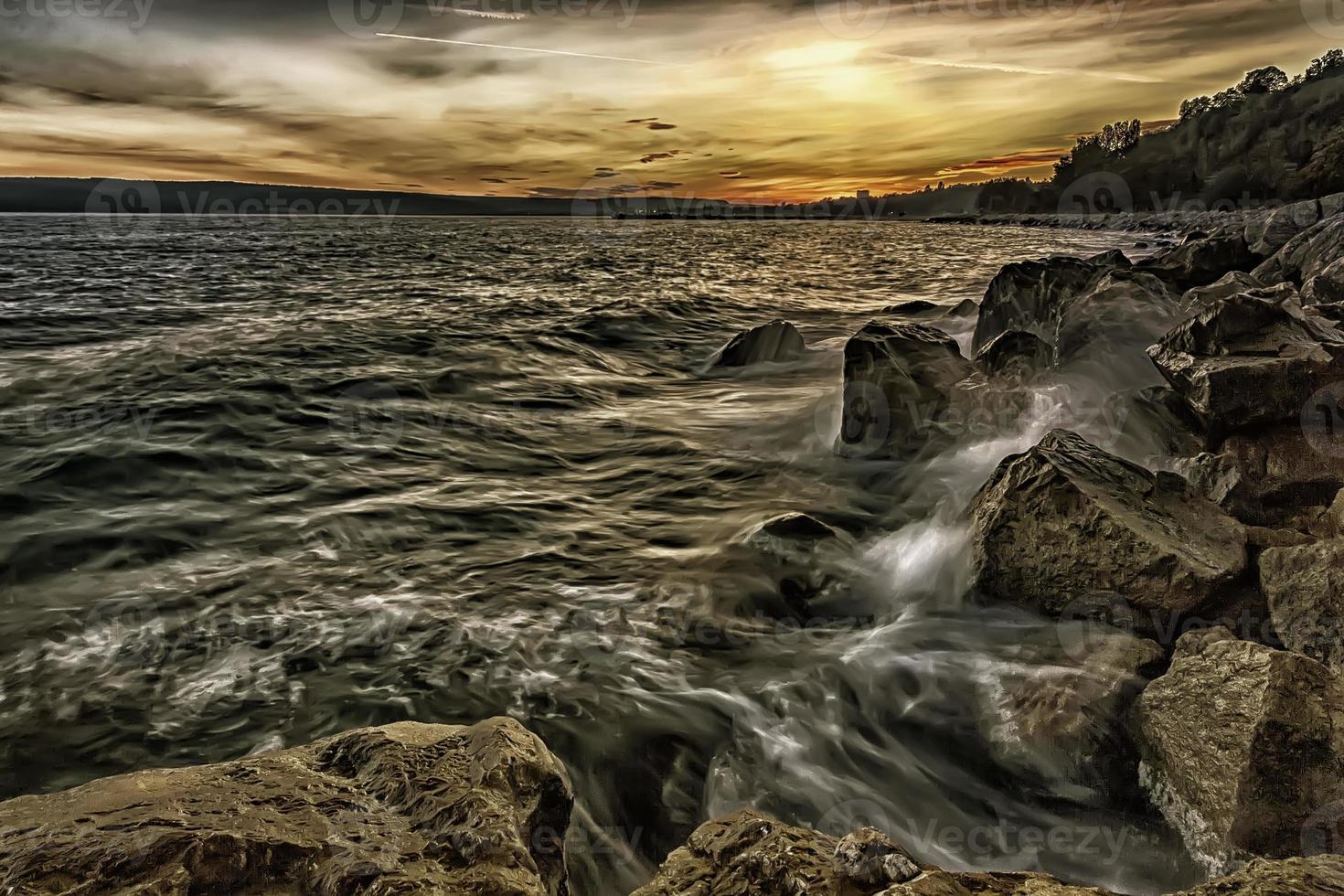solnedgång över de hav med stänk vågor på de stenar foto