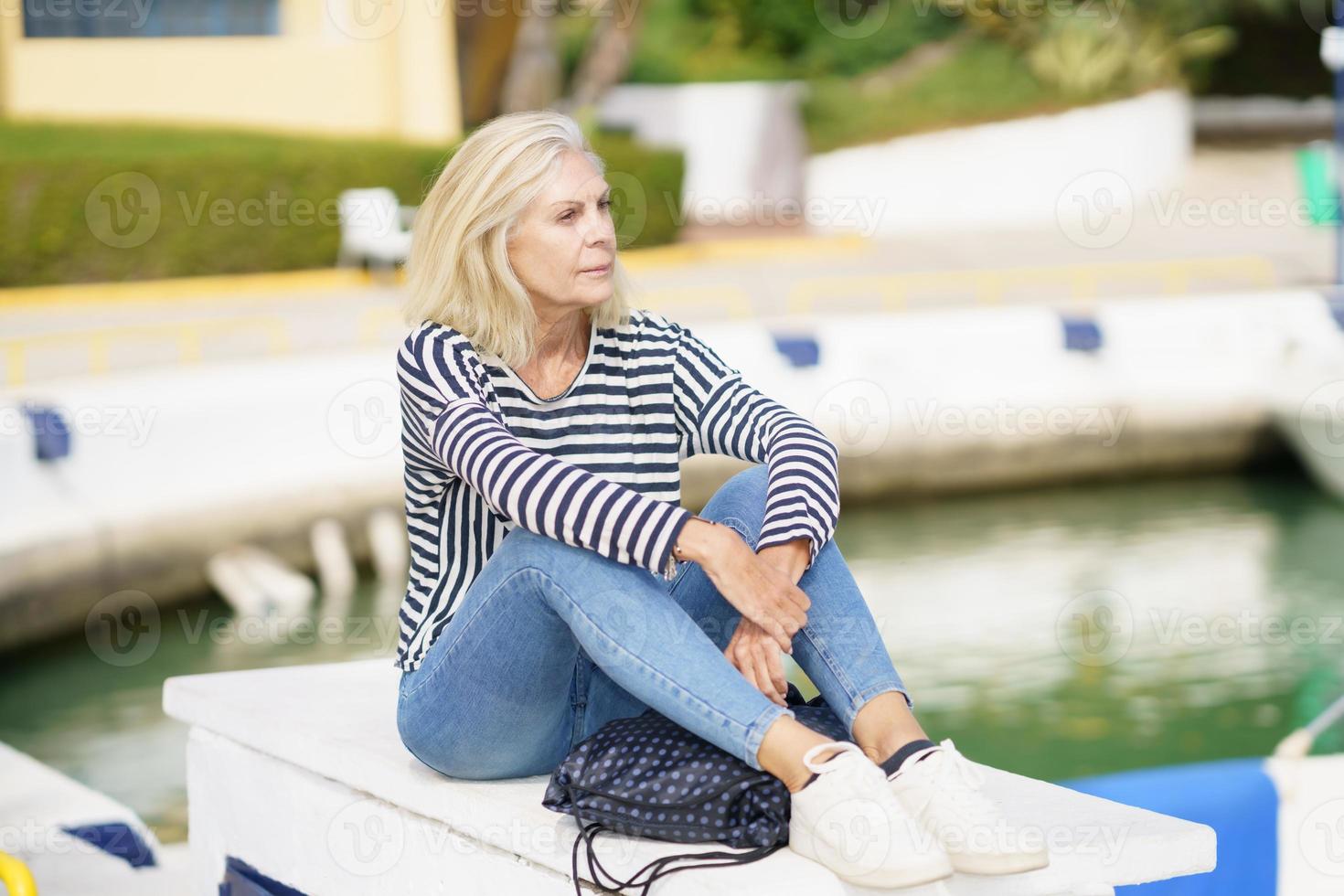 äldre kvinna tittar lugnt på kameran, sitter i en hamn. foto