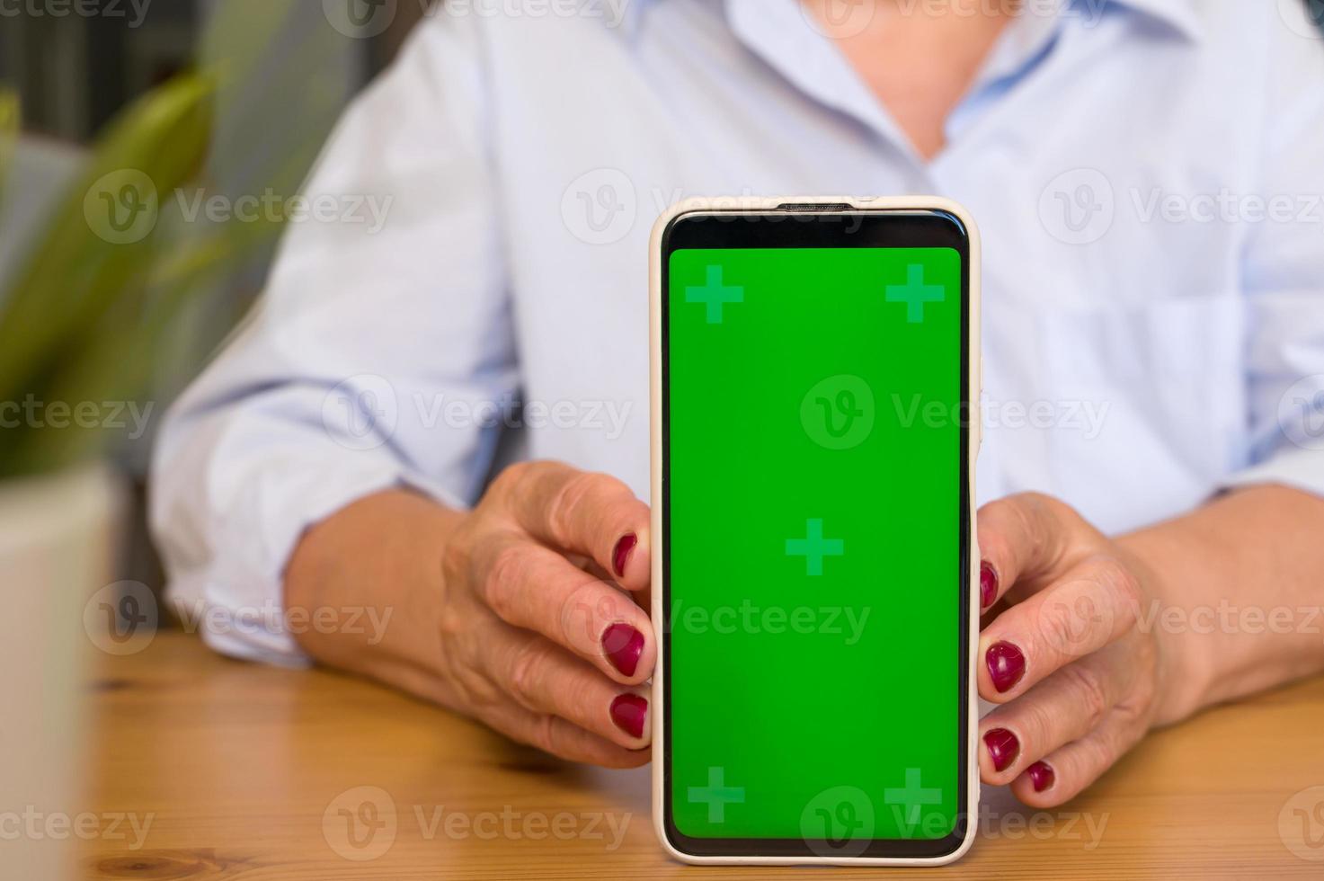 fokus på mobil telefon, oigenkännlig senior kvinna som visar grön skärm mobil telefon begrepp av uppkopplad app eller service befordran och annons. foto