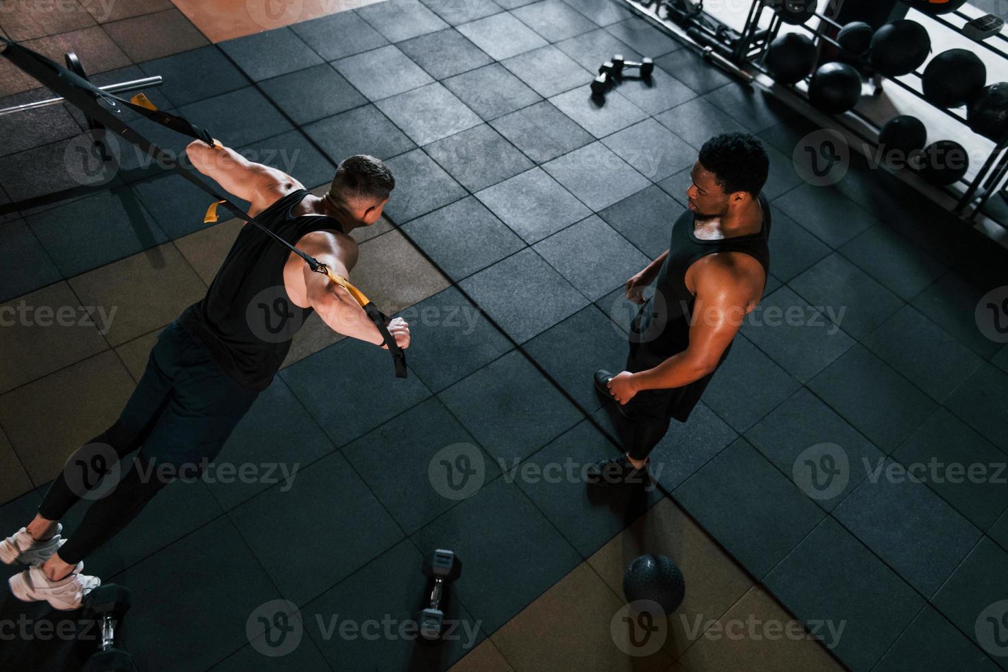 personlig tränare är på jobb. afrikansk amerikan man med vit kille ha träna dag i Gym foto