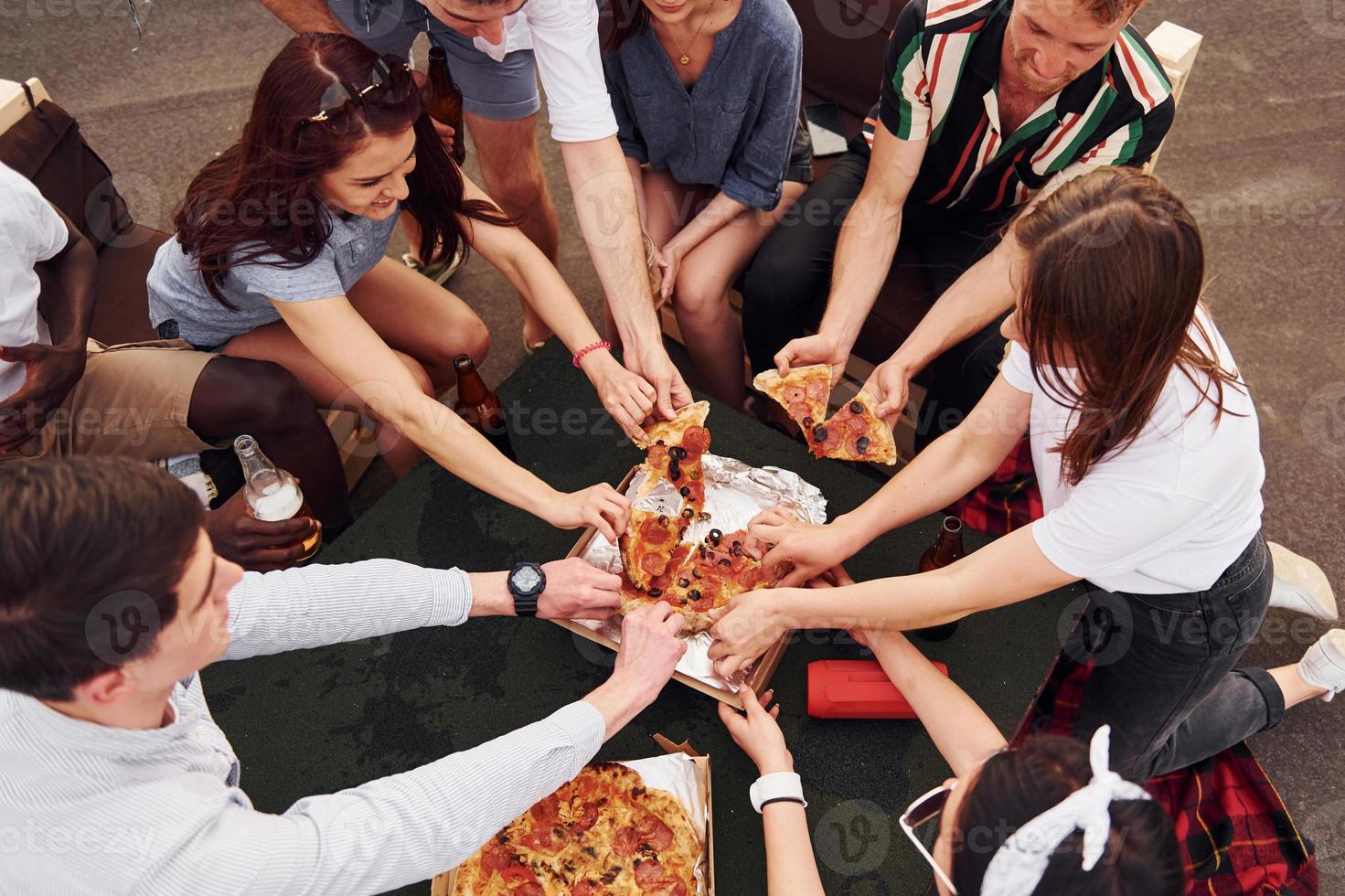 med utsökt pizza. grupp av ung människor i tillfällig kläder ha en fest på taket tillsammans på dagtid foto