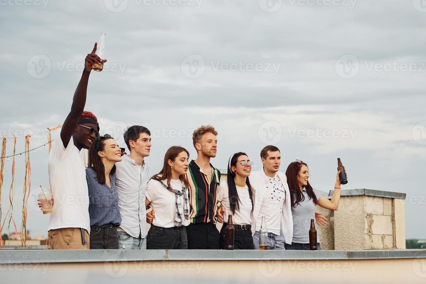 dekorerad plats. molnig väder. grupp av ung människor i tillfällig kläder ha en fest på taket tillsammans på dagtid foto