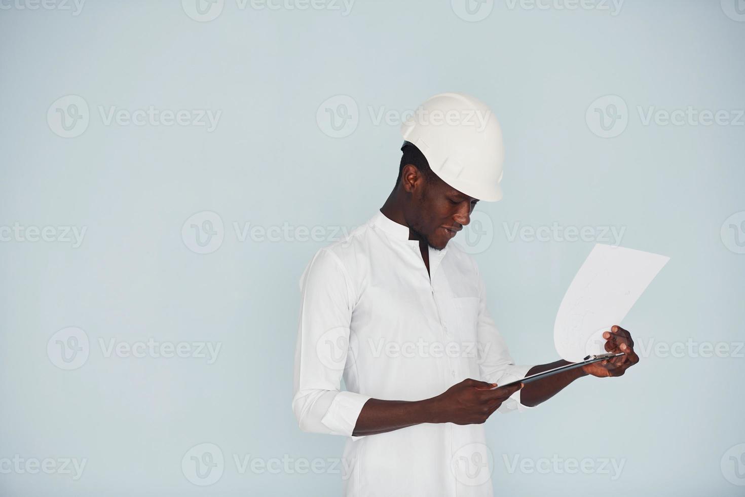 ung afrikansk amerikan ingenjör i Hardhat inomhus med anteckningsblock i händer foto