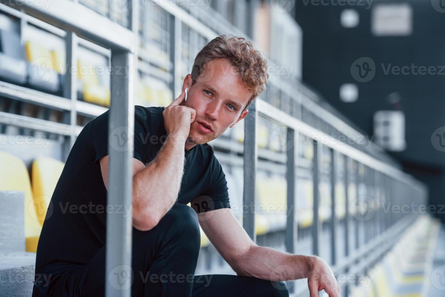 lyssnar till musik när Sammanträde. sportigt ung kille i svart skjorta och byxor utomhus på dagtid foto