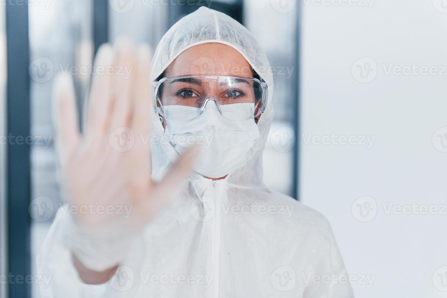 sluta de virus tecken. porträtt av kvinna läkare forskare i labb täcka, defensiv glasögon och mask foto