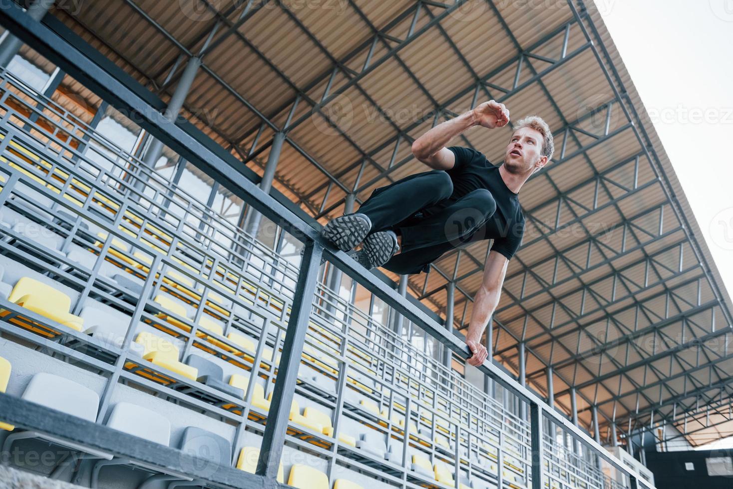 Hoppar och håller på med parkour på de läktare. sportigt ung kille i svart skjorta och byxor utomhus på dagtid foto