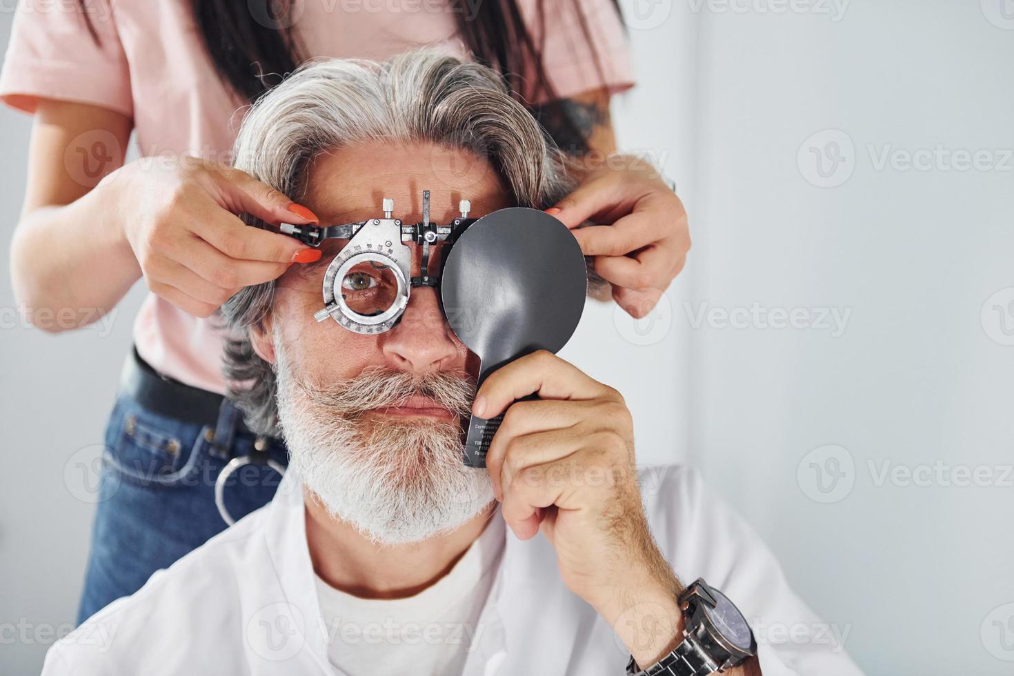 få testade förbi kvinna arbetstagare. senior man med grå hår och skägg är i oftalmologi klinik foto