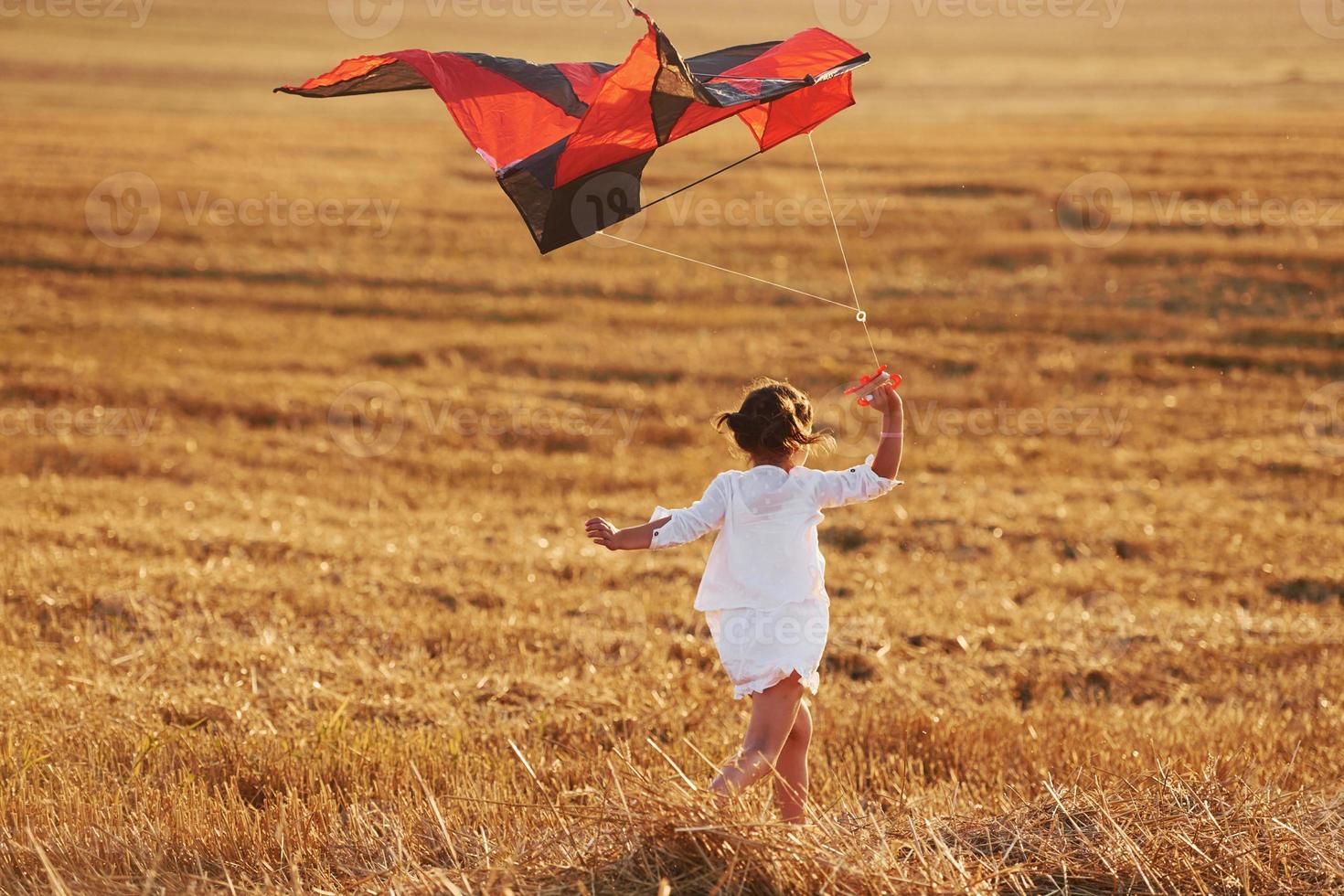 Lycklig liten flicka löpning med röd drake utomhus på de fält på sommartid foto