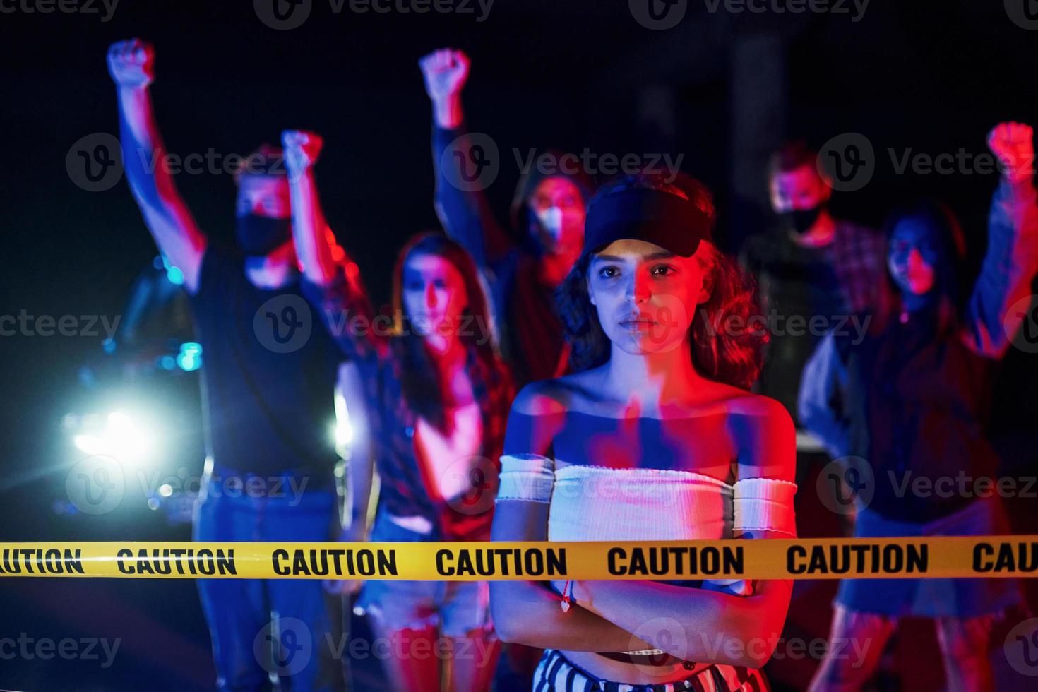 lugna kvinna stående i främre av folkmassan. grupp av protesterar ung människor den där stående tillsammans. aktivist för mänsklig rättigheter eller mot regering foto