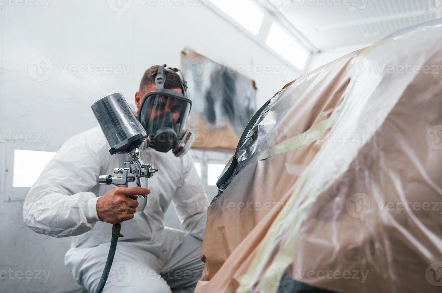 målning jobb i framsteg. caucasian bil reparatör i enhetlig Arbetar i garage foto