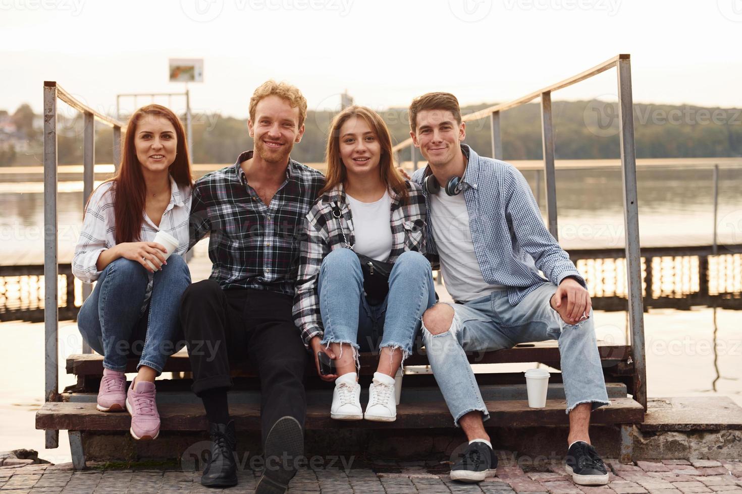 Sammanträde nära sjö och fattande varje Övrig. grupp av ung glad vänner den där är utomhus har roligt tillsammans foto