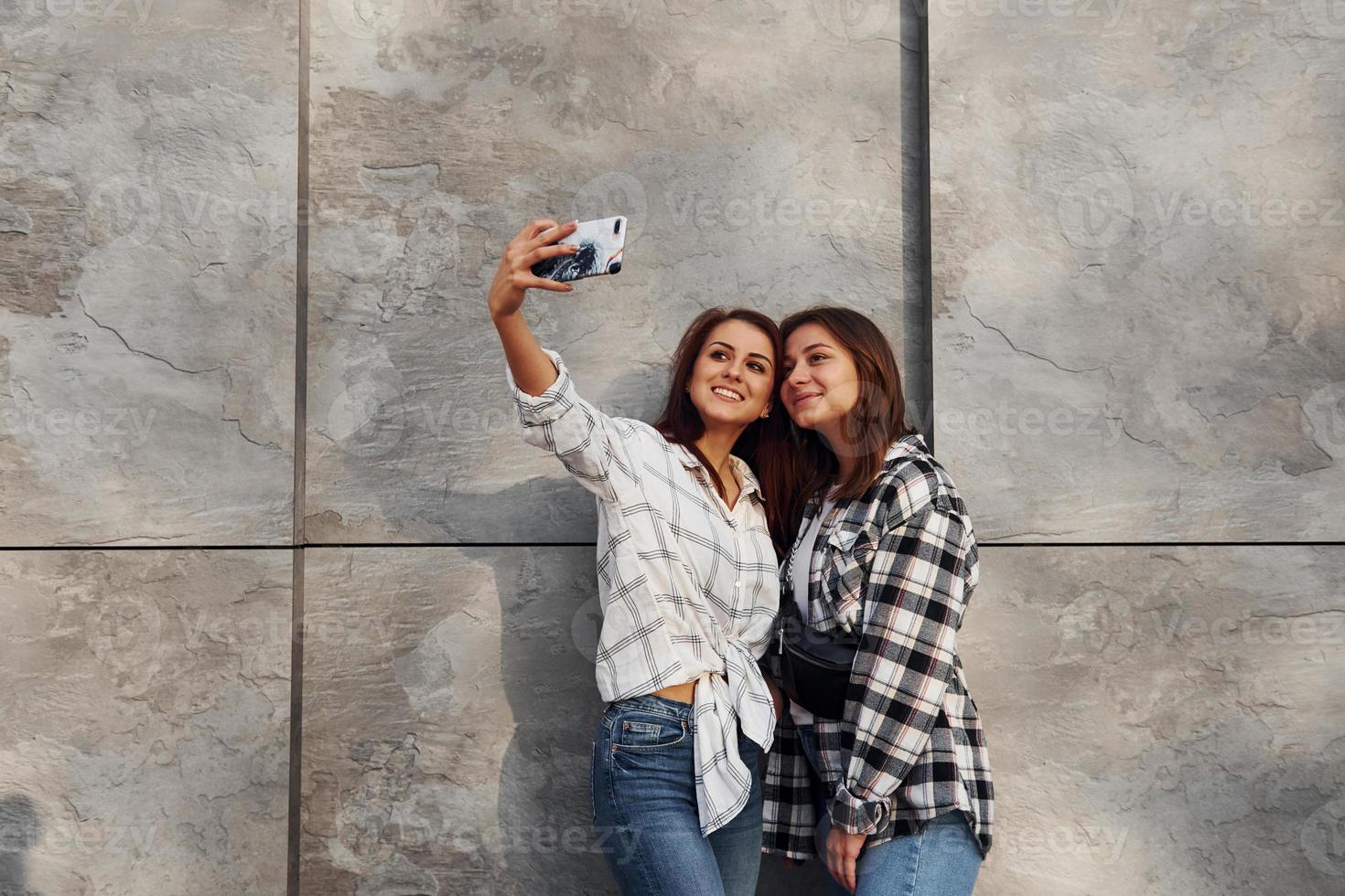 framställning selfie. skön glad vänner eller lesbisk par tillsammans nära vägg utomhus på dagtid foto