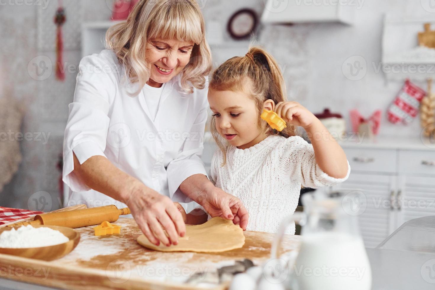 senior mormor med henne liten barnbarn kockar sötsaker för jul på de kök foto