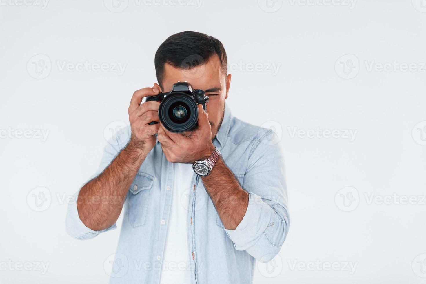 med professionell kamera. ung stilig man stående inomhus mot vit bakgrund foto