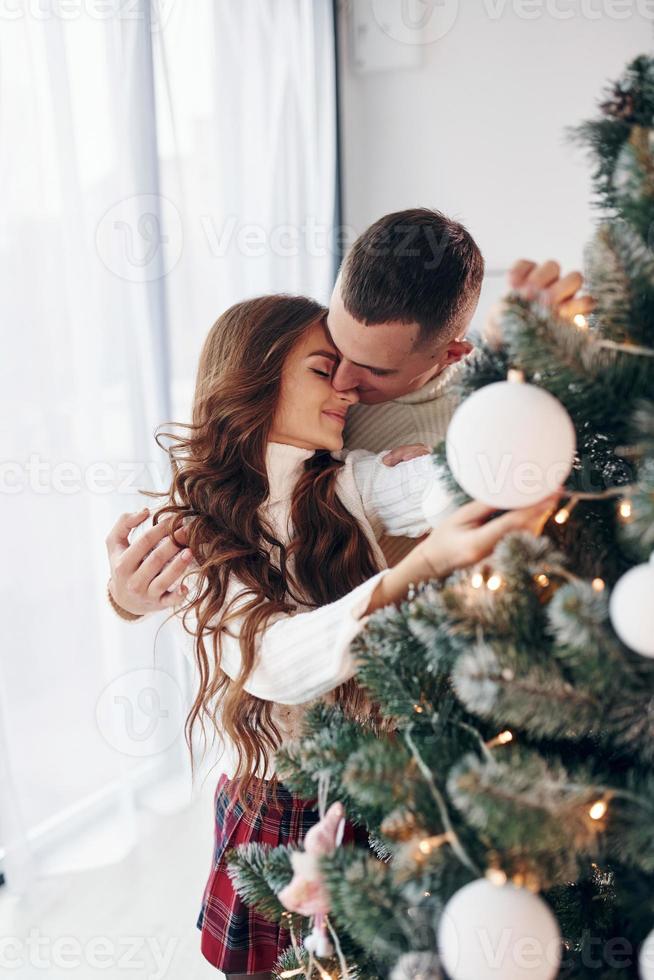stående nära gran. ung romantisk par firar ny år tillsammans inomhus foto
