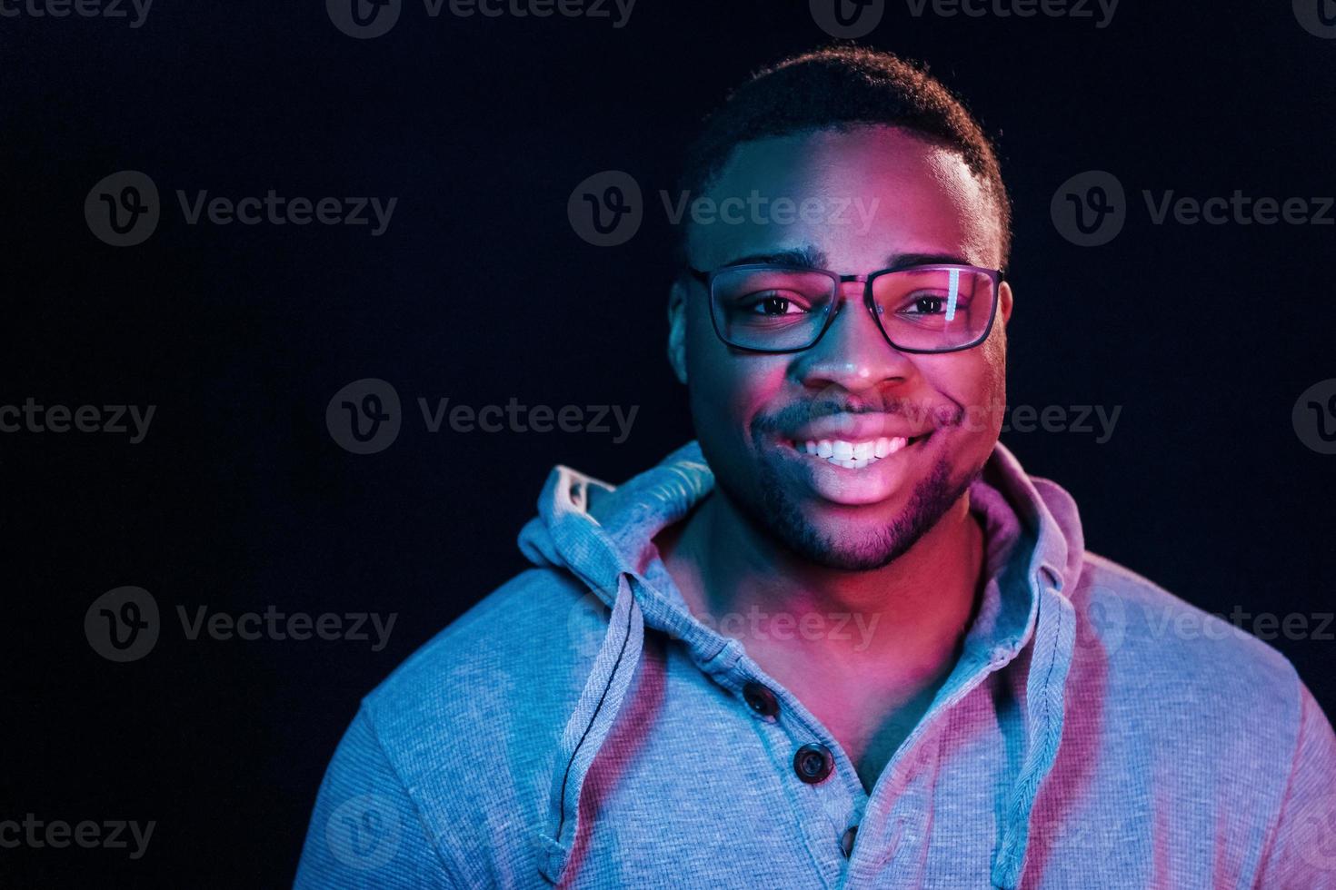 uppriktig leende. trogen neon belysning. ung afrikansk amerikan man i de studio foto