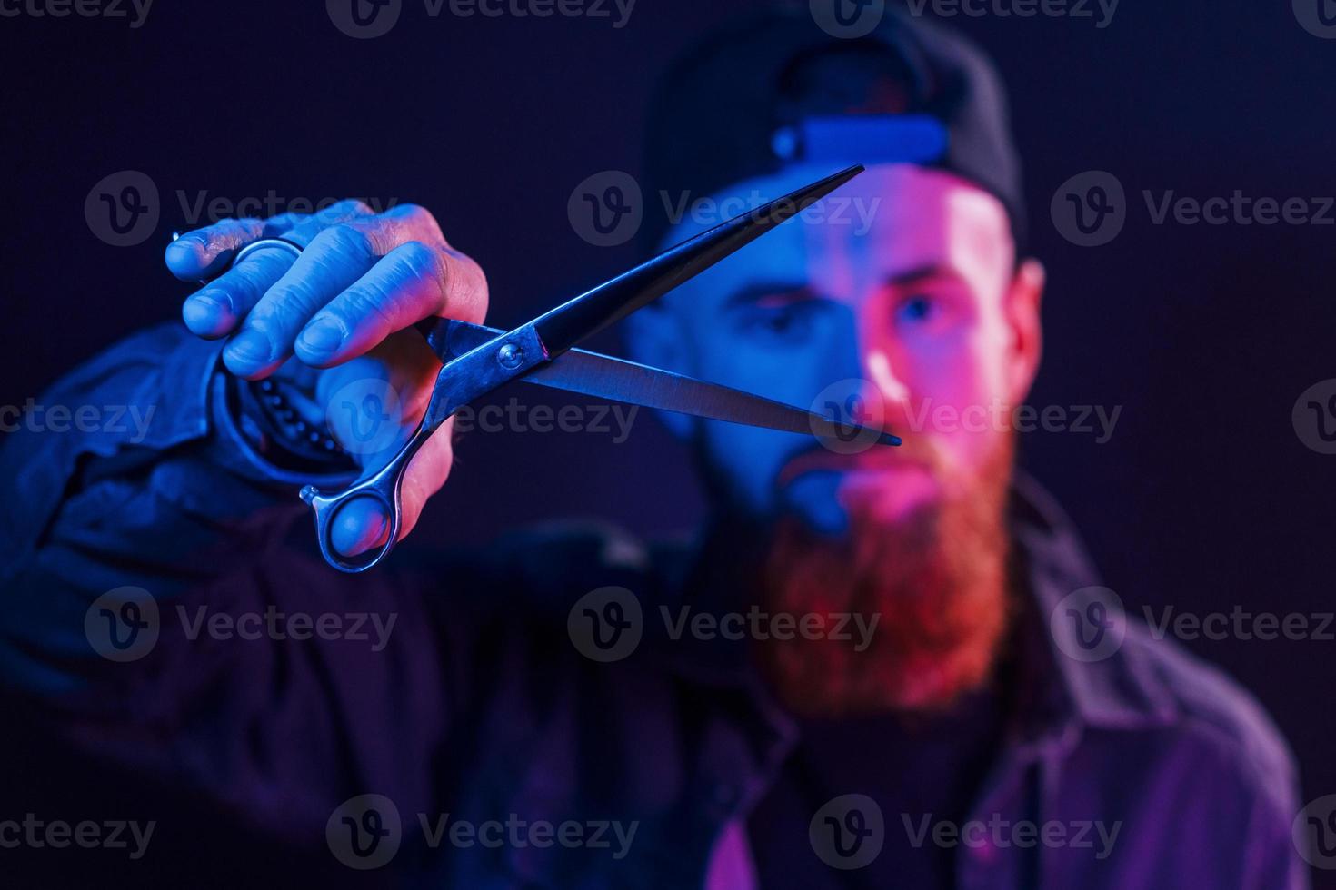 med sax. ung skäggig barberare i keps stående i de studio med neon belysning foto