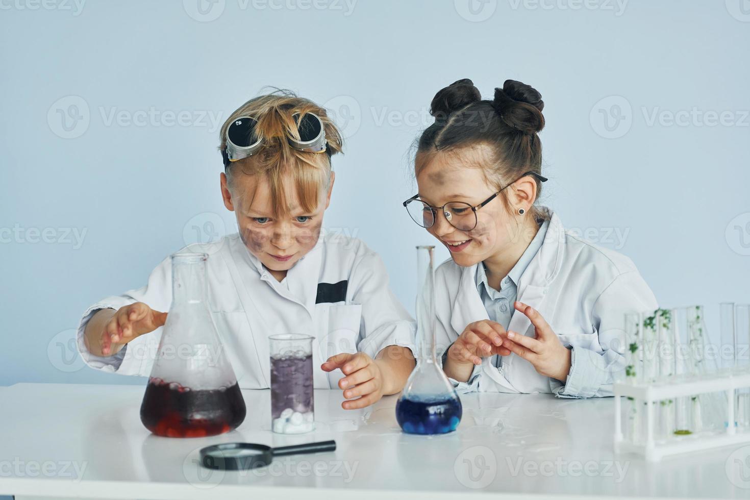 liten flicka och pojke i vit rockar spelar en vetenskapsmän i labb förbi använder sig av Utrustning foto