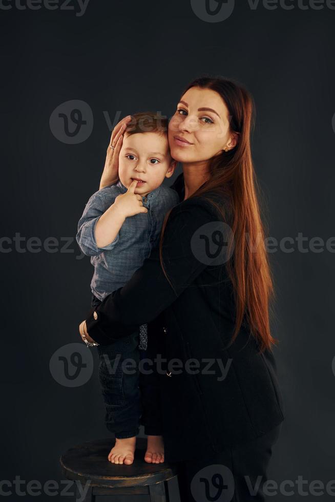 mor i eleganta svart kläder är med henne liten son i de studio foto