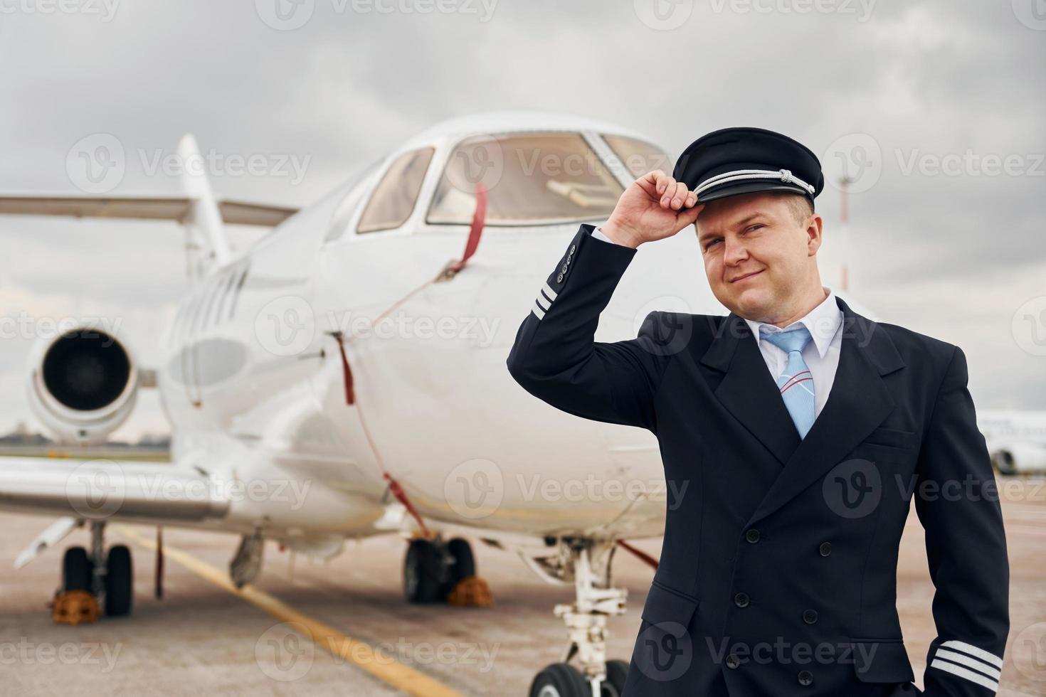 Framställ för en kamera. erfaren pilot i enhetlig stående utanför nära plan foto