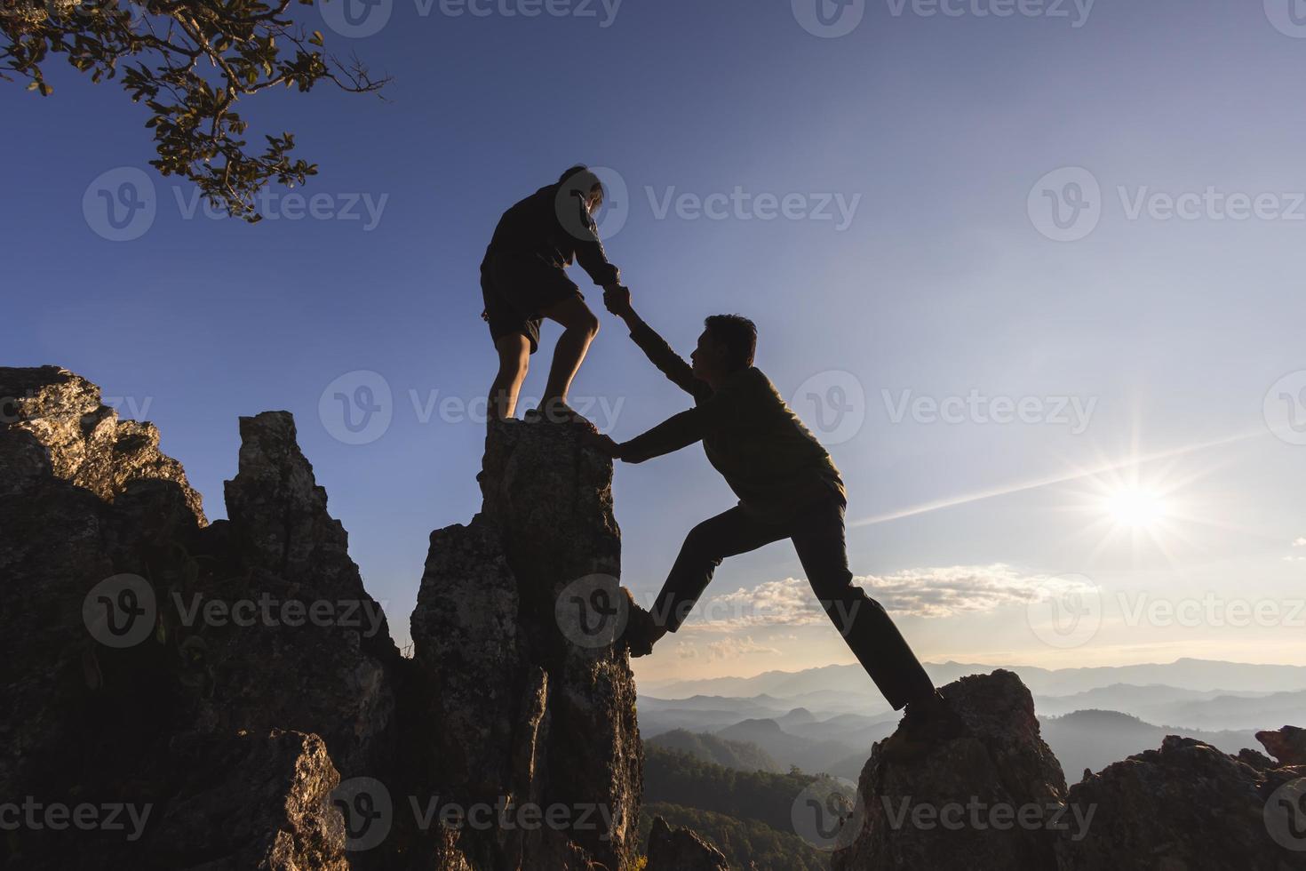 silhuett av två människor klättrande på berg klippa och ett av dem ger portion hand. människor portion och, team arbete begrepp. foto