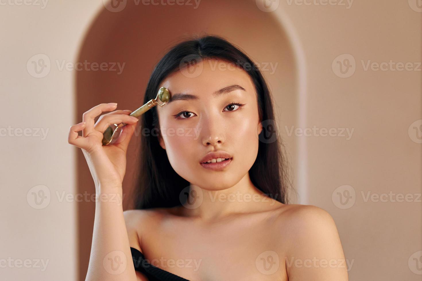 verktyg för rengöring hud. ung allvarlig asiatisk kvinna stående inomhus foto