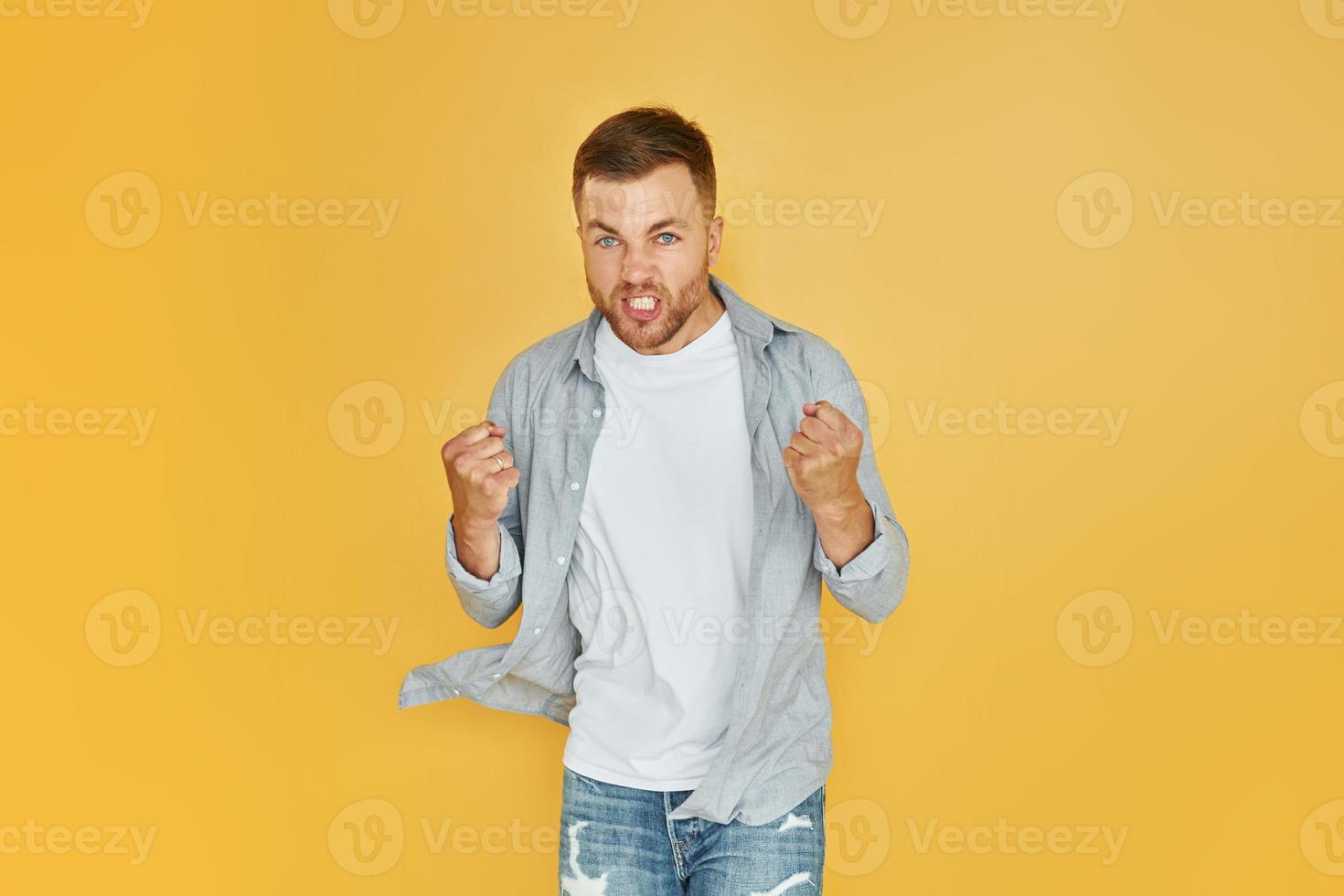 föll ilska. ung man i tillfällig kläder stående inomhus i de studio foto