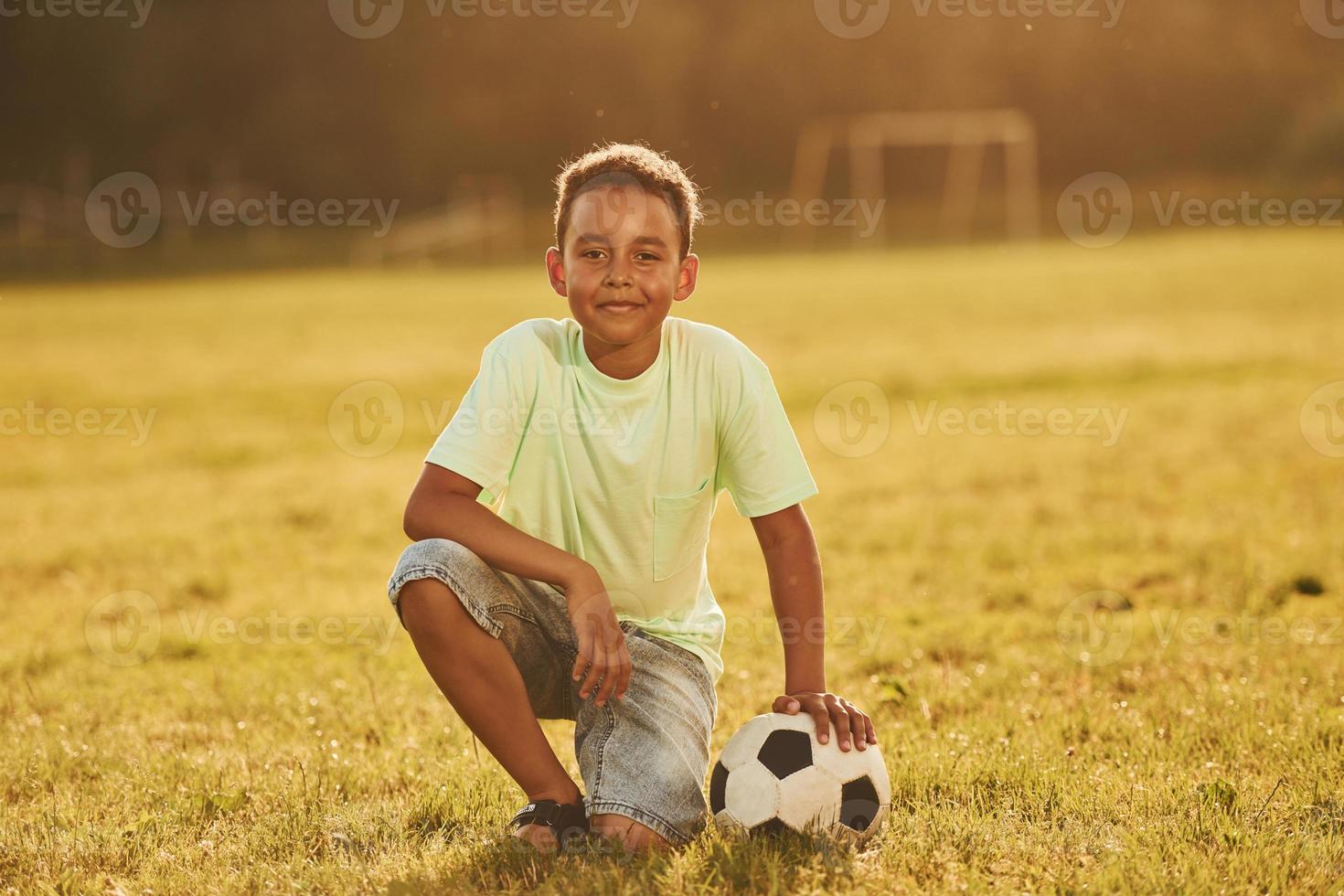 sitter med fotboll boll. afrikansk amerikan unge ha roligt i de fält på sommar dagtid foto