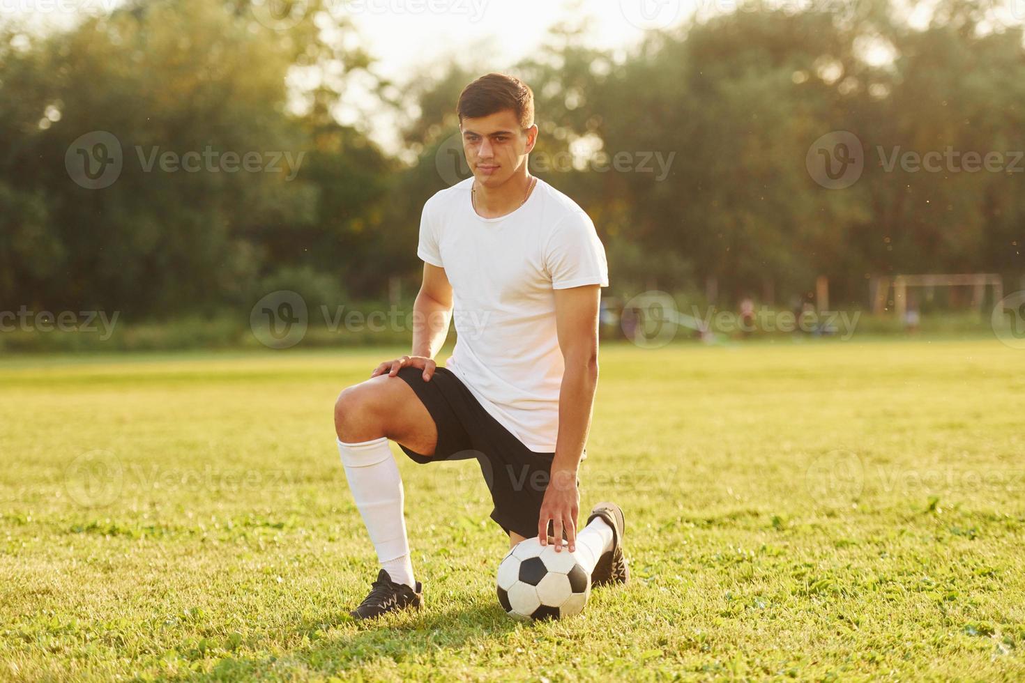 sitter på de knä med boll. ung fotboll spelare ha Träning på de sportigt fält foto