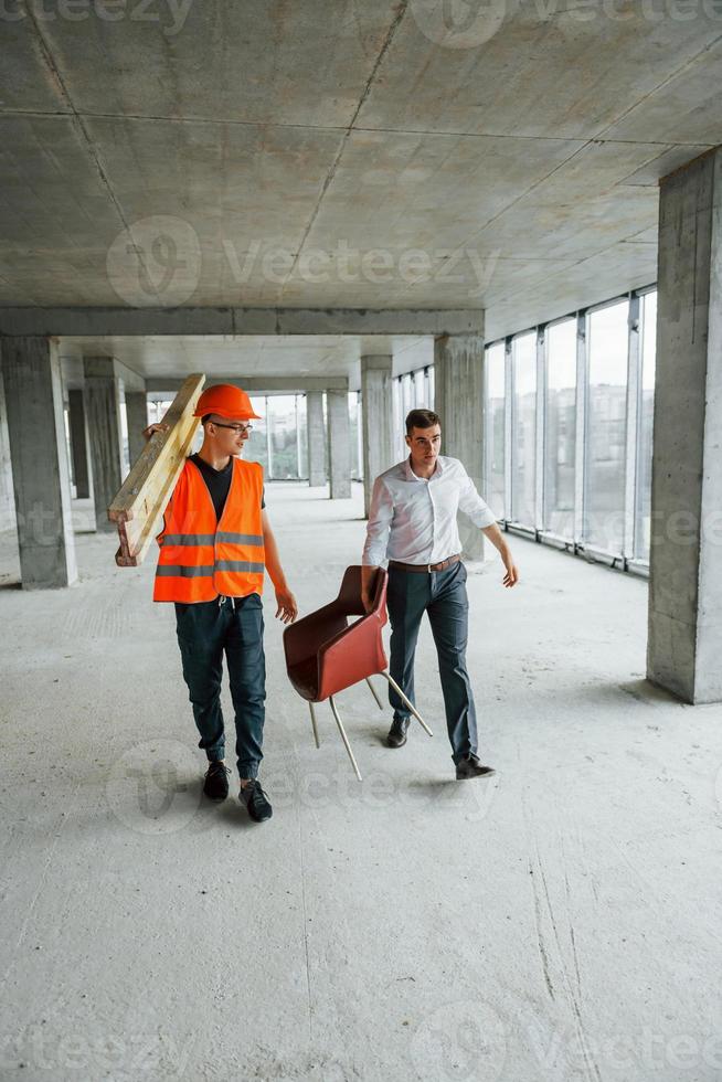 uppfattning av lagarbete. man i kostym och hantlangare i orange skyddande ha på sig är arbetssätt på konstruktion foto