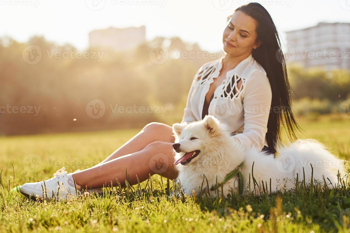 kvinna har en resten på de jord av fält med henne söt vit hund foto